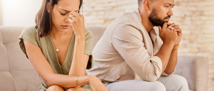 A couple sits on a sofa, their concerned looks and turned-away postures reflecting the worry and importance of securing a financial future post-divorce.