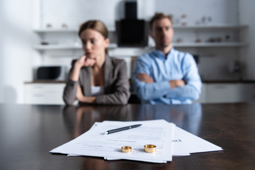 A divorcing couple sits at a table in a law office, with divorce papers and their wedding bands prominently placed before them, representing the complexities of a high net worth divorce.