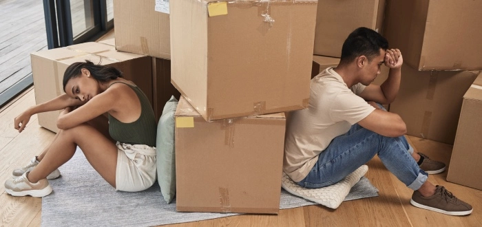 
A divorced couple sits on the floor amidst packed boxes, symbolizing their transition into new living arrangements and the start of separate lives.