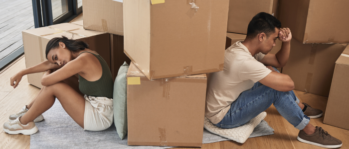 A divorced couple sits on the floor amidst packed boxes, symbolizing their transition into new living arrangements and the start of separate lives.