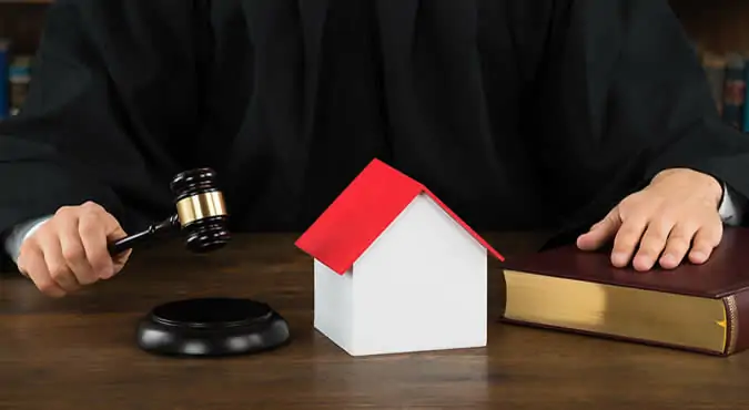 A model house next to a gavel on a desk, symbolizing the legal and personal implications of leaving the marital home.