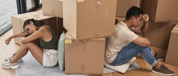 A couple sits on the floor amidst moving boxes, a somber representation of the uncertainty and legal implications when one spouse leaves the marital home.