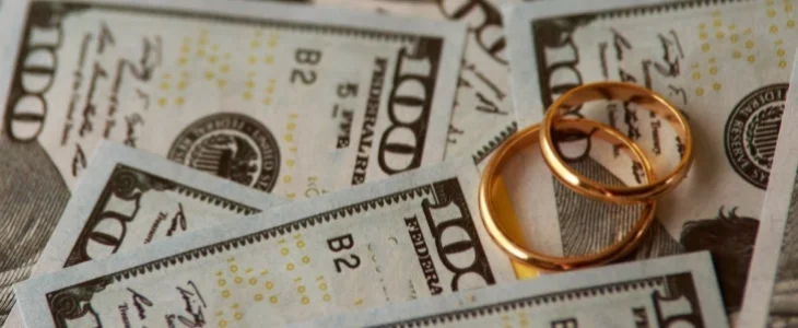 Wedding rings laying atop a pile of cash money, encapsulating the critical exploration of what a wife is entitled to in divorce settlements.
