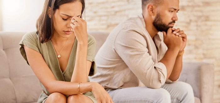 A couple sits on a sofa, their concerned looks and turned-away postures reflecting the worry and importance of securing a financial future post-divorce.