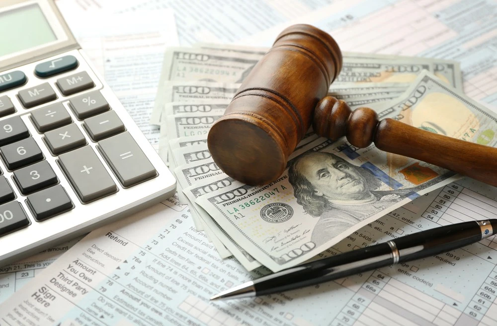 A calculator, financial documents, cash, and a gavel lay on a desk, symbolizing the effort to bridge the gap between two health insurance plans.