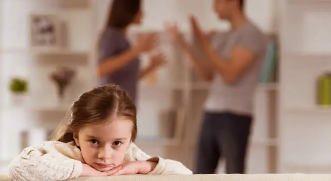 A child looks on with sadness as their parents argue vehemently in the room, underscoring the urgent need for a lawyer and court-decided custody.