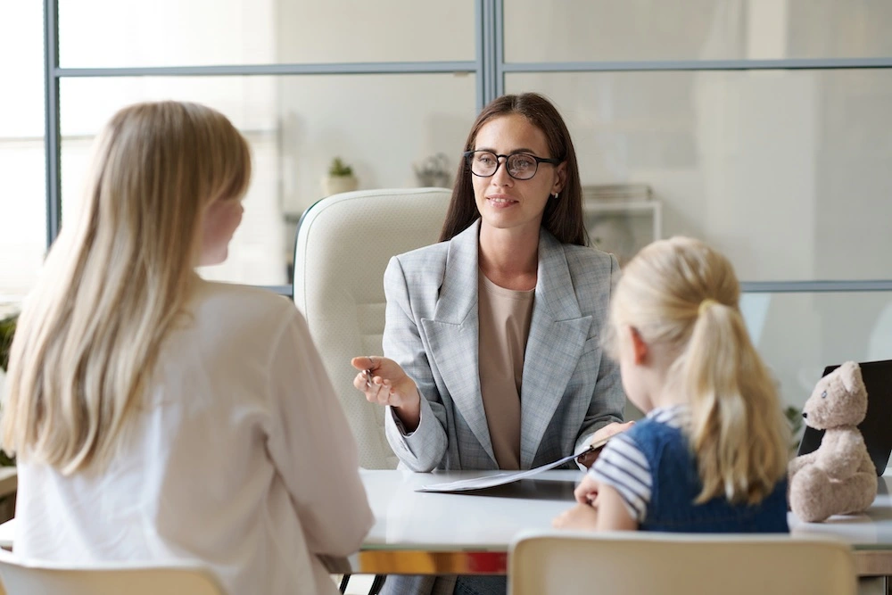 A mother sits next to her child in an office, engaging in a serious discussion with a family lawyer about child custody arrangements.